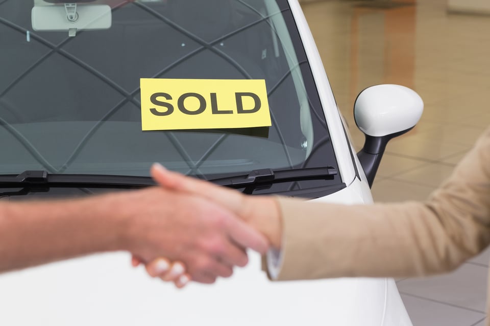 Person shaking hands in front of a sold car at new car showroom